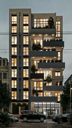 a very tall building with lots of windows and plants on the balconies at night