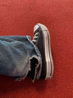 a person's feet with ripped jeans and black shoes on the floor in front of a red carpet