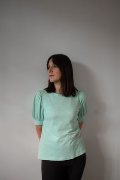 a woman standing in front of a white wall wearing black pants and a green top