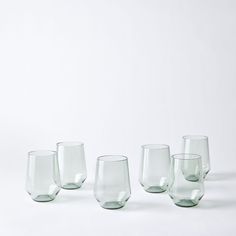 five glasses are lined up on a white surface, with one empty glass in the middle