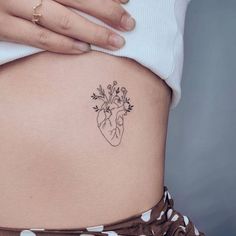 a woman's stomach with a small heart tattoo on the lower belly and flowers growing out of it