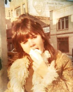 a woman eating something while standing in front of a building