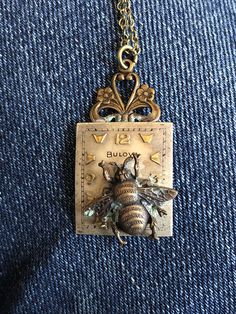 a necklace with a bee on it hanging from a gold plated chain and attached to a blue jean jacket