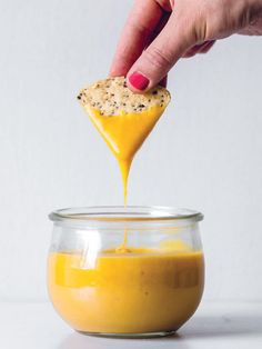 a person is dipping something into a glass bowl with orange sauce in it and there are other ingredients on the table