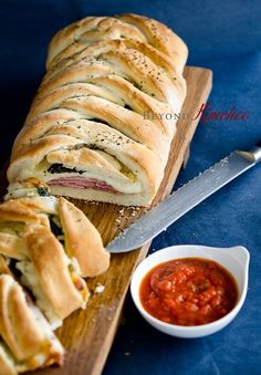 a sandwich cut in half on a cutting board next to a bowl of tomato sauce