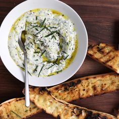 a white bowl filled with dip and grilled bread on top of a wooden table