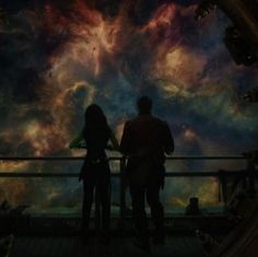 two people standing in front of a colorful sky with clouds and stars on the ceiling