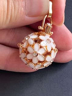 a close up of a person's hand holding a small ball shaped pendant with flowers on it