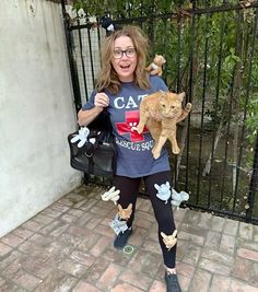 a woman holding an orange cat in her arms and wearing leggings with cats on them