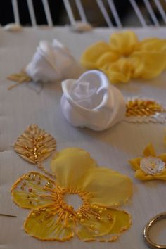 yellow and white fabric flowers on a table with two gold wedding rings next to them