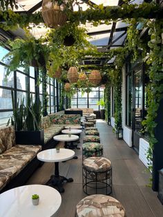 an indoor seating area with plants and potted plants on the ceiling, along with white tables and chairs