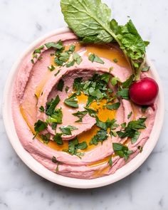 a bowl filled with hummus and garnish next to a radish