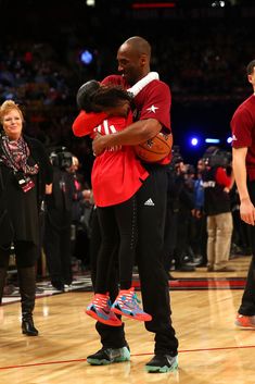 two basketball players hug each other on the court as people watch from the sidelines