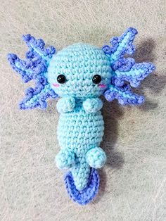 a crocheted blue stuffed animal laying on top of a white blanket