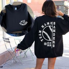 a woman is walking down the street wearing a black sweatshirt with baseball stitches on it