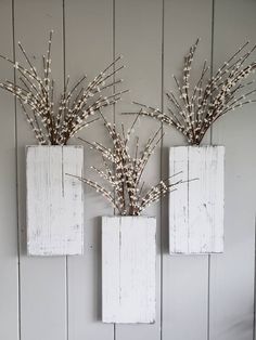 three white square vases with branches in them on a shelf next to a wall