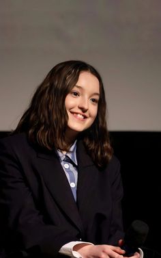 a woman in a suit and tie is smiling at the camera while holding a microphone