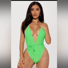 a woman in a green one piece swimsuit with her hand on her chest, posing for the camera