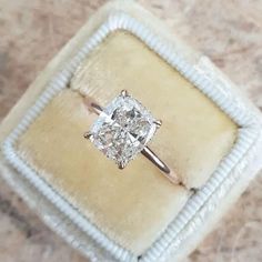 an engagement ring with a cushion cut diamond in it sitting on a velvet box,