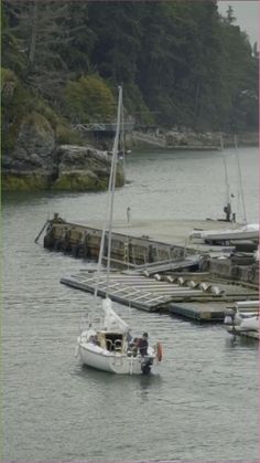 a small sailboat in the water next to a dock with several smaller boats on it