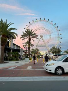 a white car driving down a street next to tall palm trees and a ferris wheel