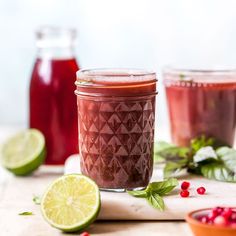 two jars filled with liquid and garnished with limes, pomegranates and mint