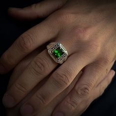 a close up of a person's hand wearing a ring with a green stone