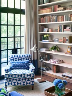 a living room filled with lots of books on top of white shelving units next to a window