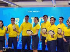 a group of people standing next to each other in front of a blue wall holding hats