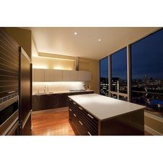 an empty kitchen with large windows overlooking the city lights at night in this modern apartment