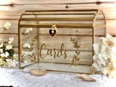 a glass box with the word cards in it and flowers around it on a lace tablecloth