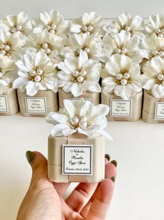 a hand holding a small gift box with white flowers on it and the label says,