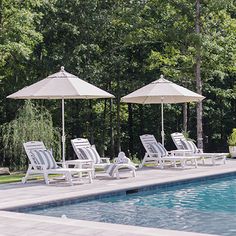 several lawn chairs and umbrellas near a pool with trees in the backgroud