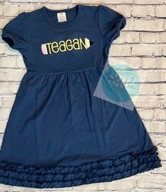 a blue dress with the word teagan on it, against a white brick wall