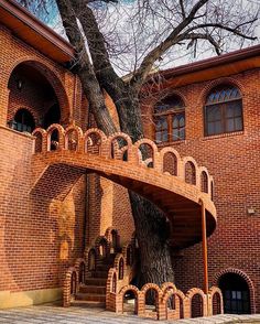 an old brick building with a large tree in the front and stairs leading up to it