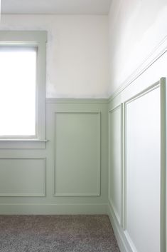 an empty room with green paneling and white trim on the walls, along with a window