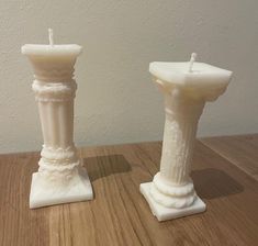 two white candles sitting on top of a wooden table next to each other with one candle in the middle