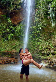 a man holding a woman in front of a waterfall while she is on her back