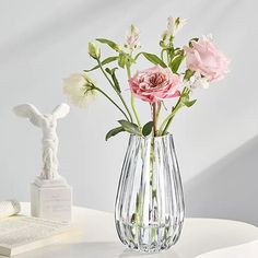 a vase filled with pink and white flowers on top of a table next to an open book