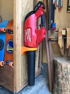 a red and black driller sitting on top of a piece of wood in a garage