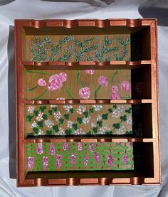 an open wooden box with flowers painted on the inside and in different shades of pink