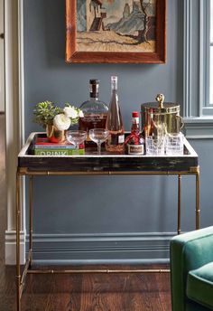 a bar cart with liquor bottles and glasses on it in front of a framed painting