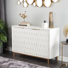 a white sideboard with gold accents and mirrors on the wall above it, along with a vase filled with flowers