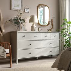 a bedroom scene with focus on the dresser and bed sideboard, potted plant and mirror