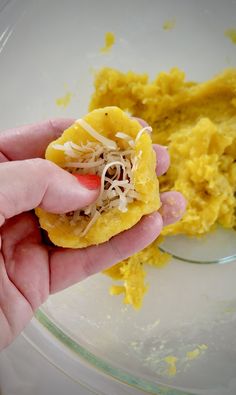 a person holding food in their hand near some yellow stuff on a plate with other food