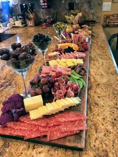 an assortment of cheeses, meats and grapes on a wooden platter with wine glasses