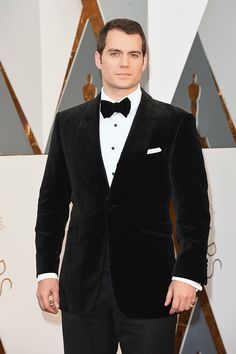 a man in a tuxedo and bow tie standing on the red carpet at an oscars event