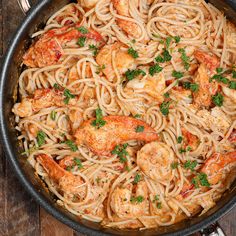 pasta with shrimp and parsley in a skillet on a wooden table next to utensils