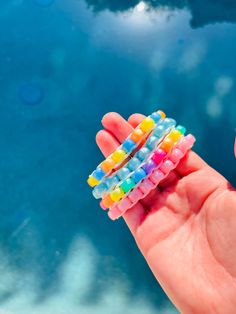 a hand holding some colorful toothbrushes in it's palm next to the ocean