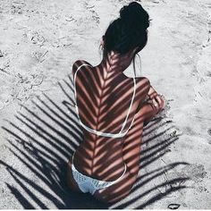 a woman sitting in the sand with her back turned to the camera, casting a shadow